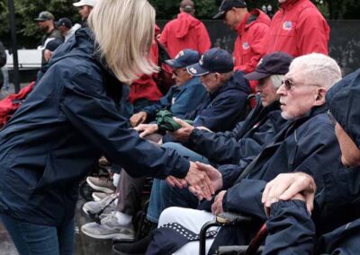 "A woman shakes hands with veterans as they board the Honor Flight, offering a heartfelt gesture of gratitude and respect for their service."