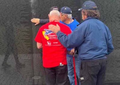 Three Honor Flight veterans standing at the Vietnam Veterans Memorial, paying tribute to fallen comrades.